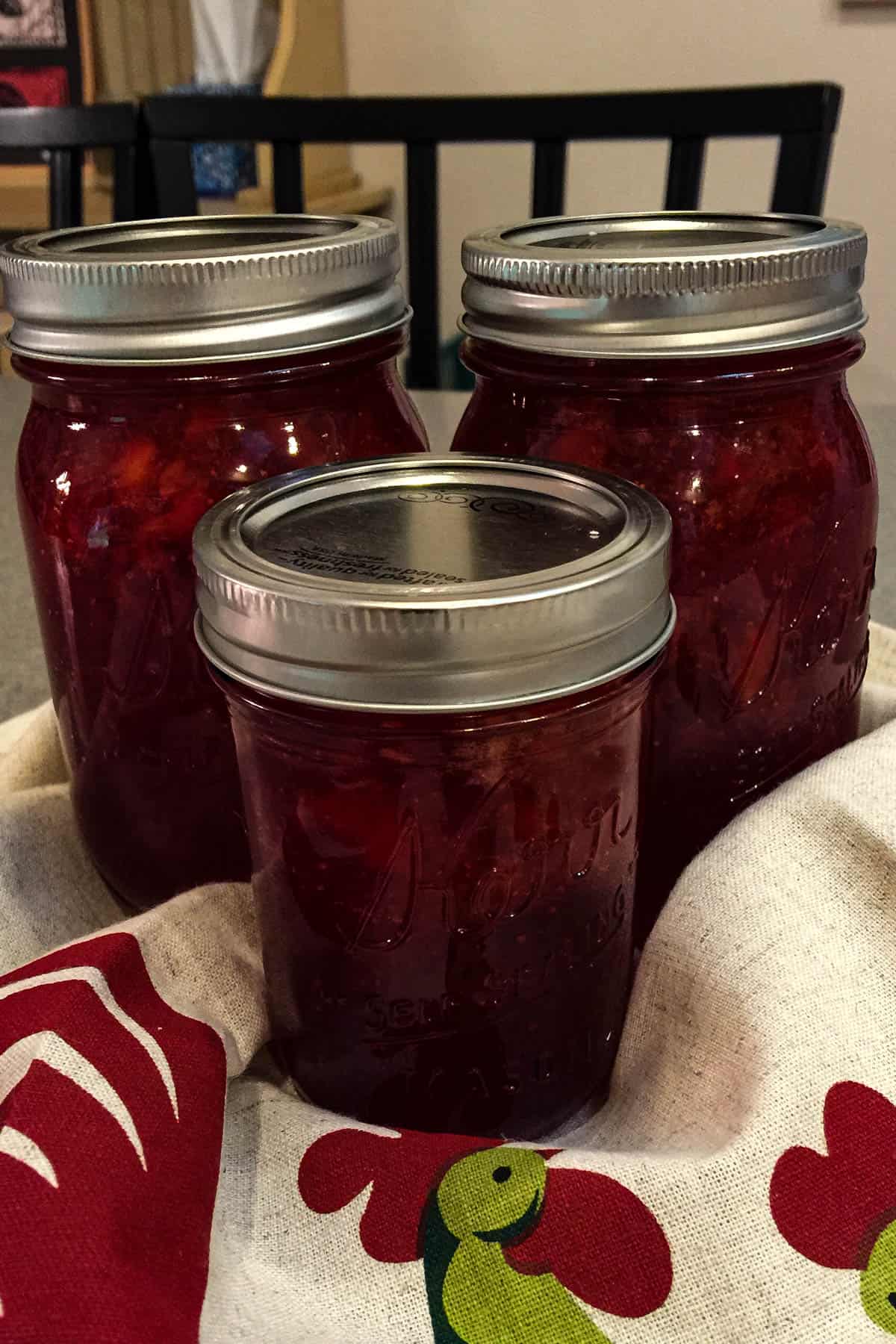 Three jars of canned strawberry jam.