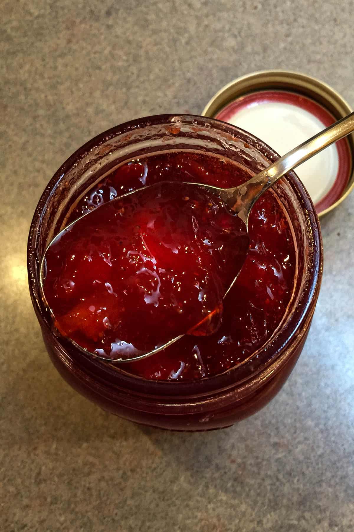 Overhead closeup of jam on spoon hovering over open jar.
