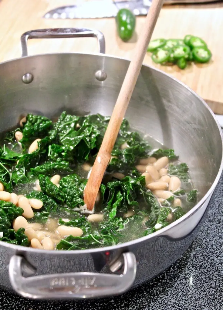 Tuscan Kale and Cannellini Bean Soup on stove cooking with wooden spoon