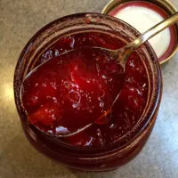 Overhead closeup of jam on spoon hovering over open jar.