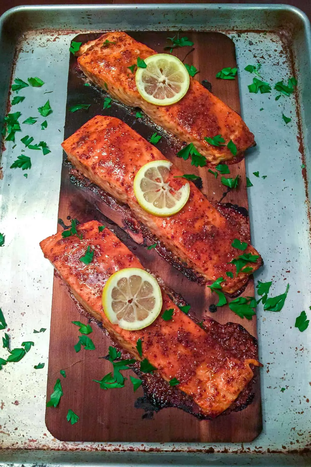 Finished cedar planked salmon garnished with lemon slices and chopped parsley.