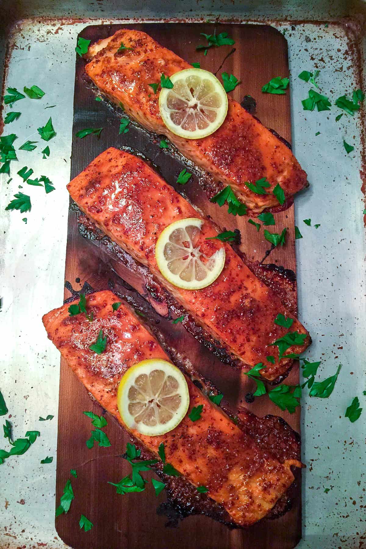 Finished cedar planked salmon garnished with lemon slices and chopped parsley.