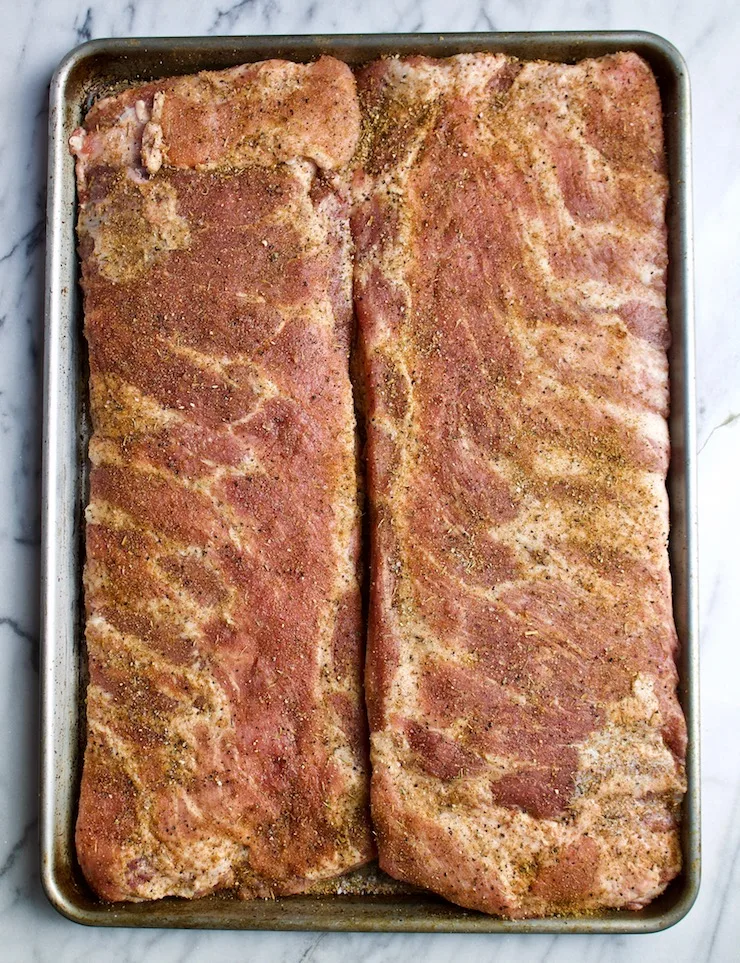 Two slabs of pork spareribs with dry rub, ready for grill.