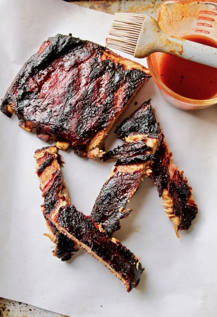 Ribs off the grill, cut into sections with basting sauce in background.