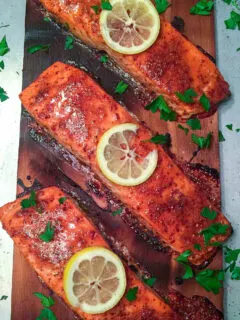 Finished cedar planked salmon garnished with lemon slices and chopped parsley.