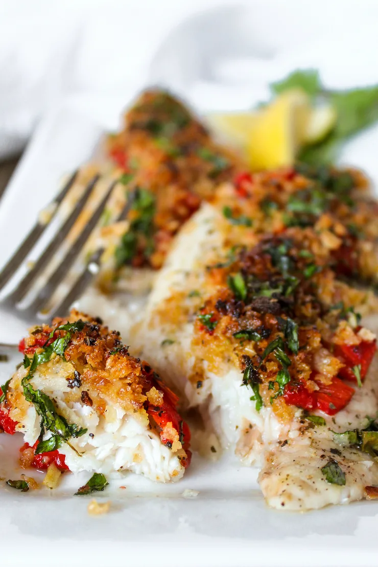 Greek white fish on plate with portion flaked with fork.