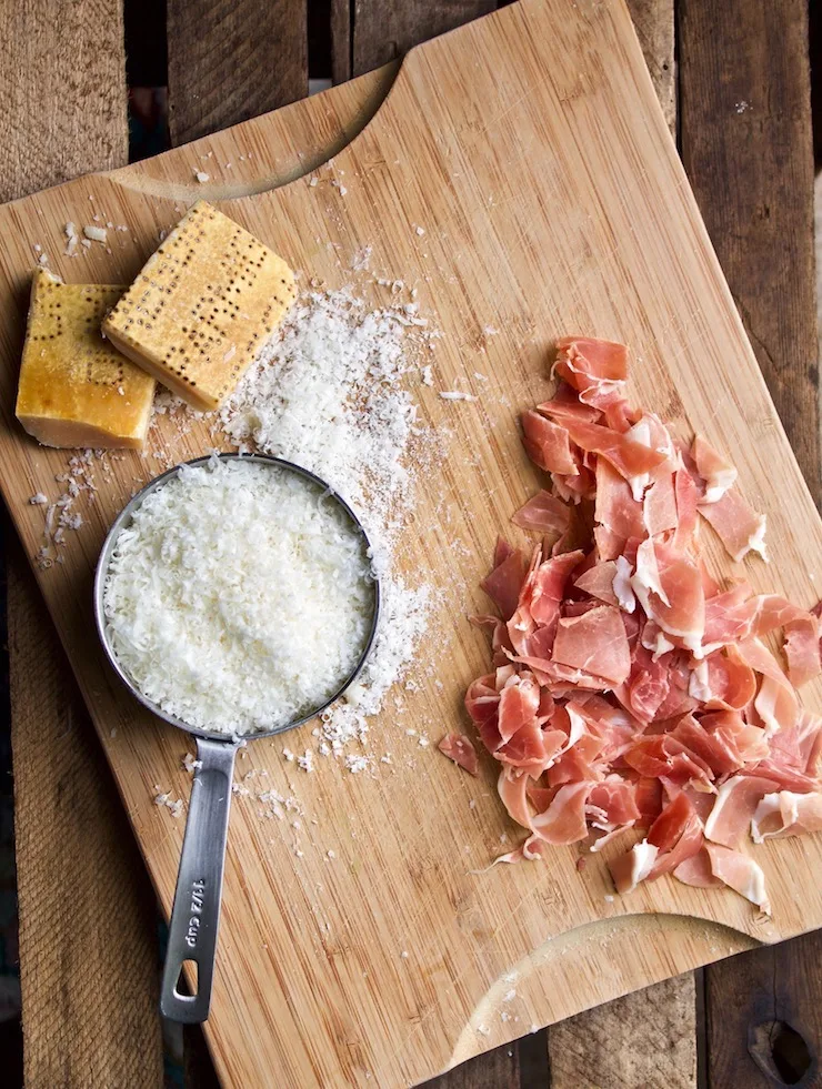 Grated parmesan and chopped prosciutto on cutting board.