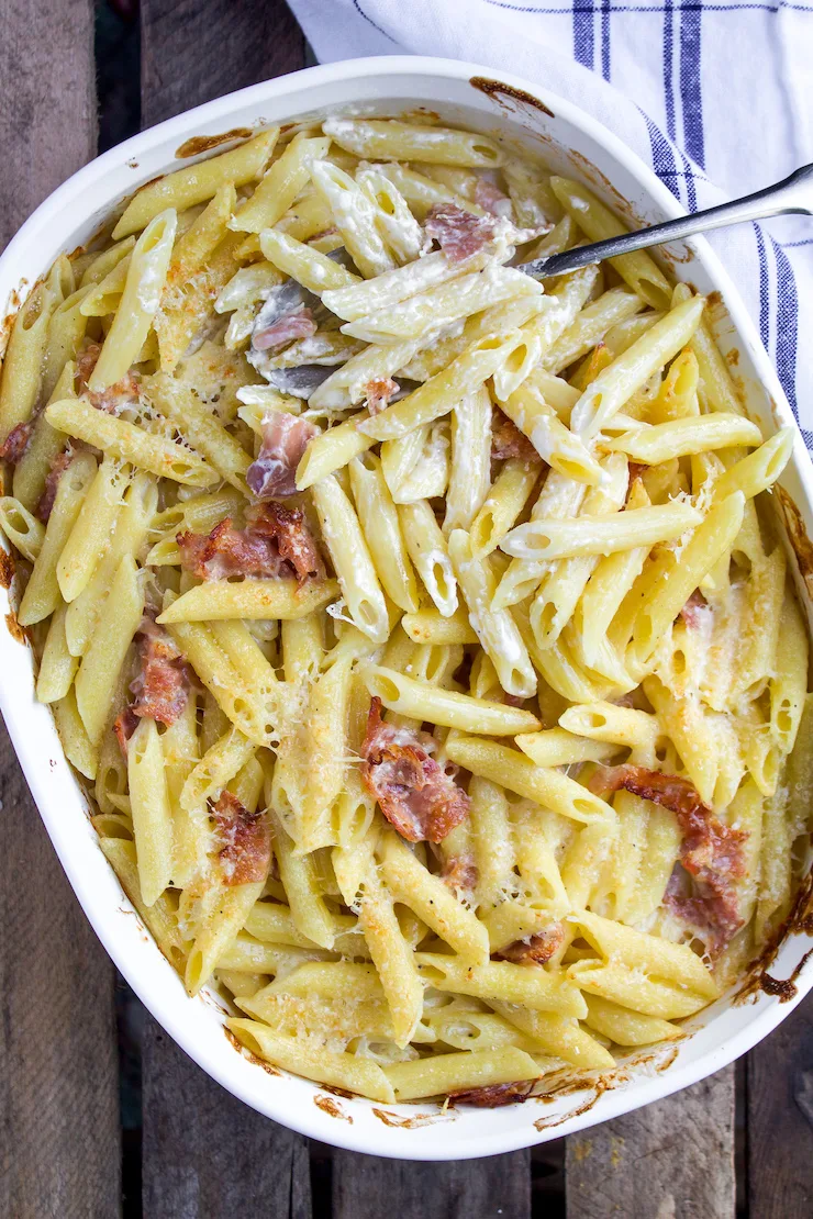Baked penne with prosciutto and Parmesan cream in casserole dish.