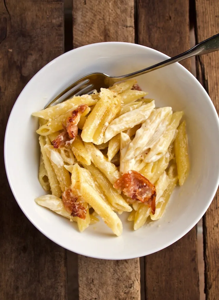 Penne with Prosciutto and Parmesan Cream in white bowl with fork.