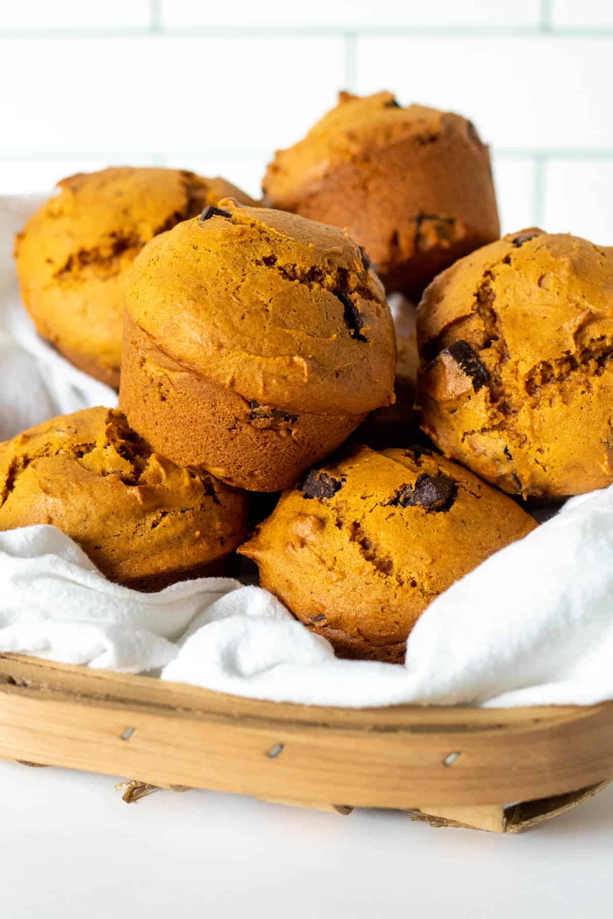 Pumpkin chocolate chip muffins in a basket lined with white towel.