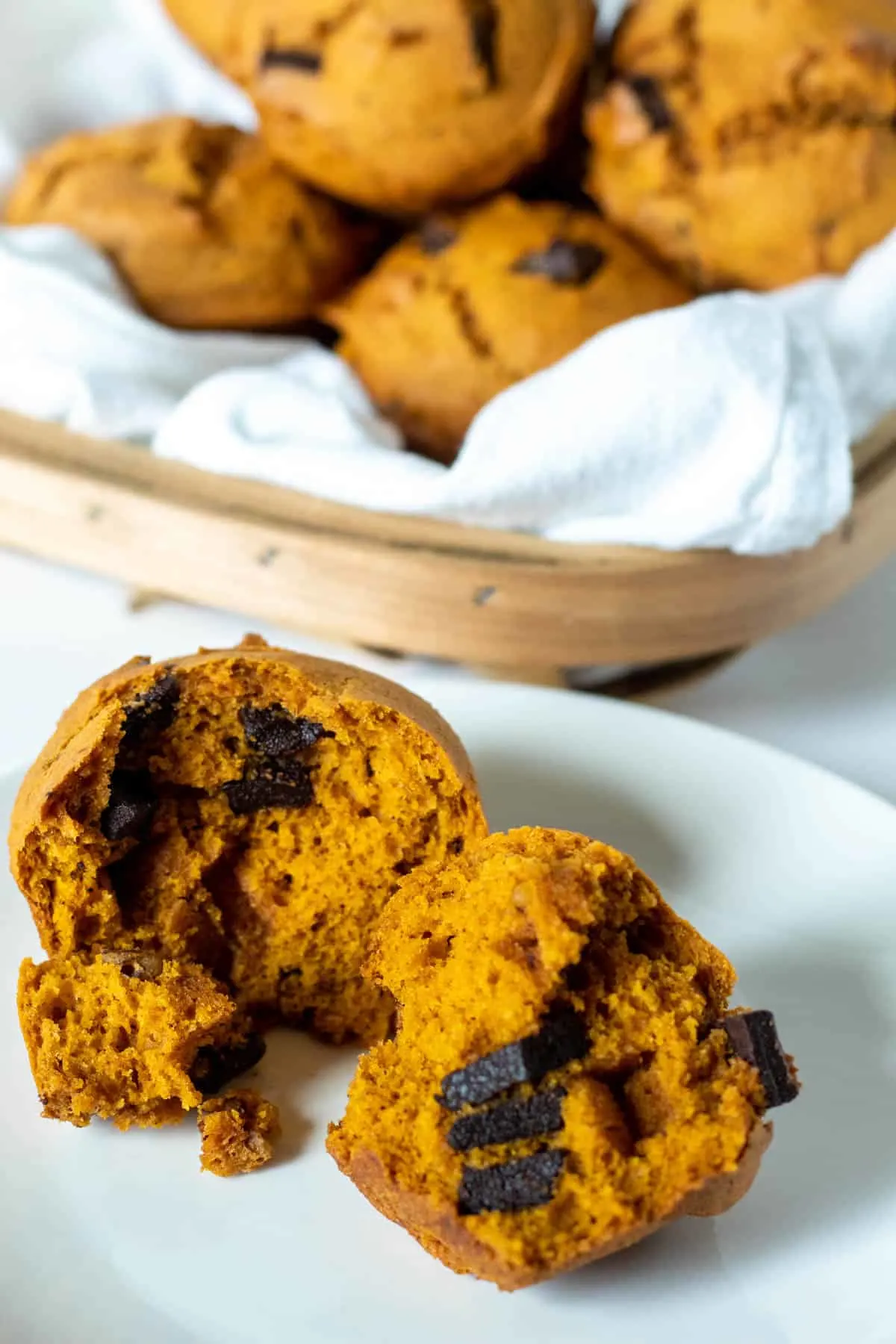 Pumpkin chocolate chip muffin on white plate with basket in background.