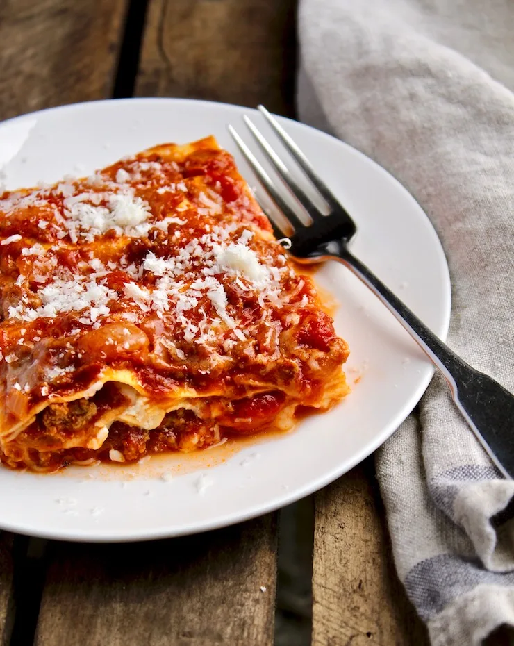 Mom's Lasagna,on a white plate with grated Parmesan and fork