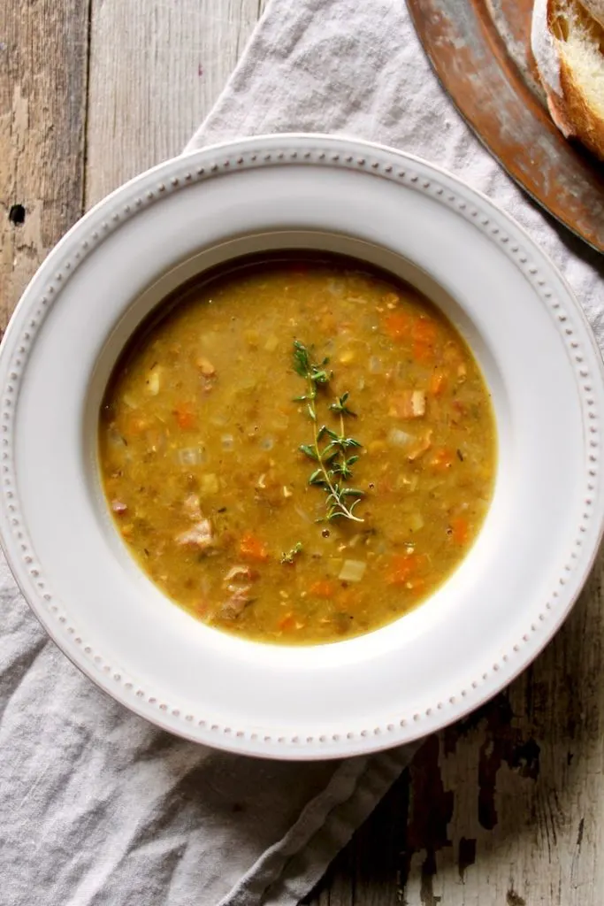Split pea soup in white bowl with thyme sprig.