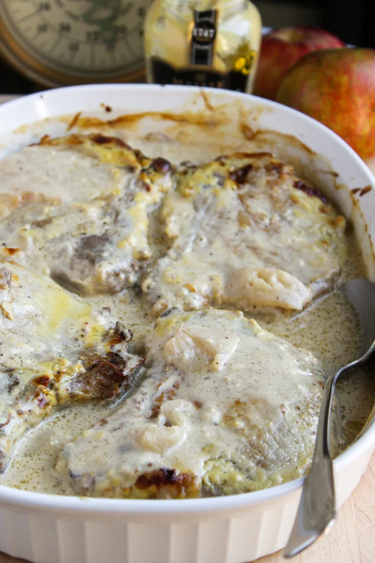 Finished pork chops and apples in baking dish with spoon.