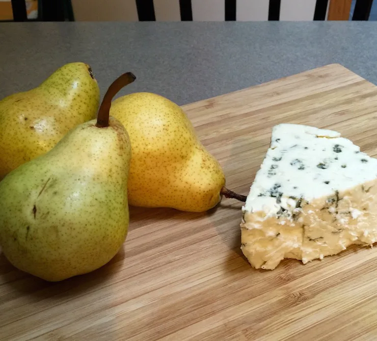 Three pears and wedge of blue cheese on cutting board.