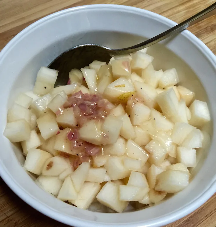 Cubed pears tossed with dressing in bowl with spoon.