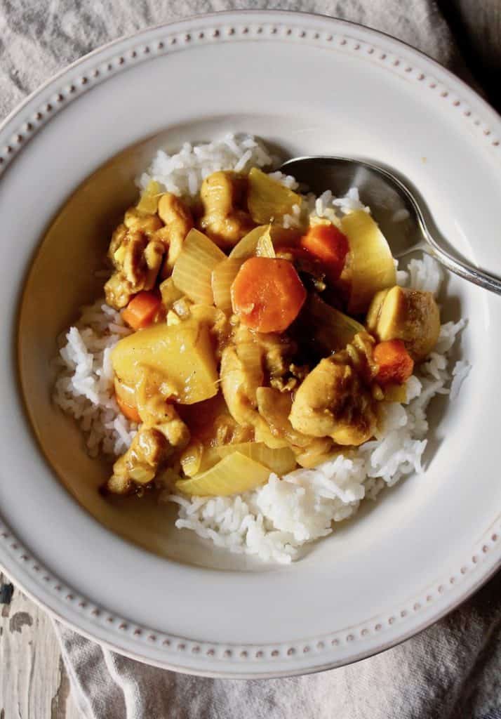 Chicken curry in bowl with rice and spoon.
