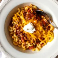 Bowl of chili over macaroni with toppings.