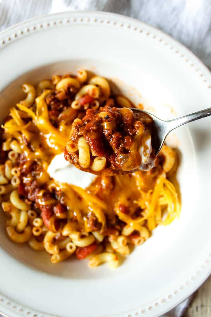Chili mac on spoon above bowl.