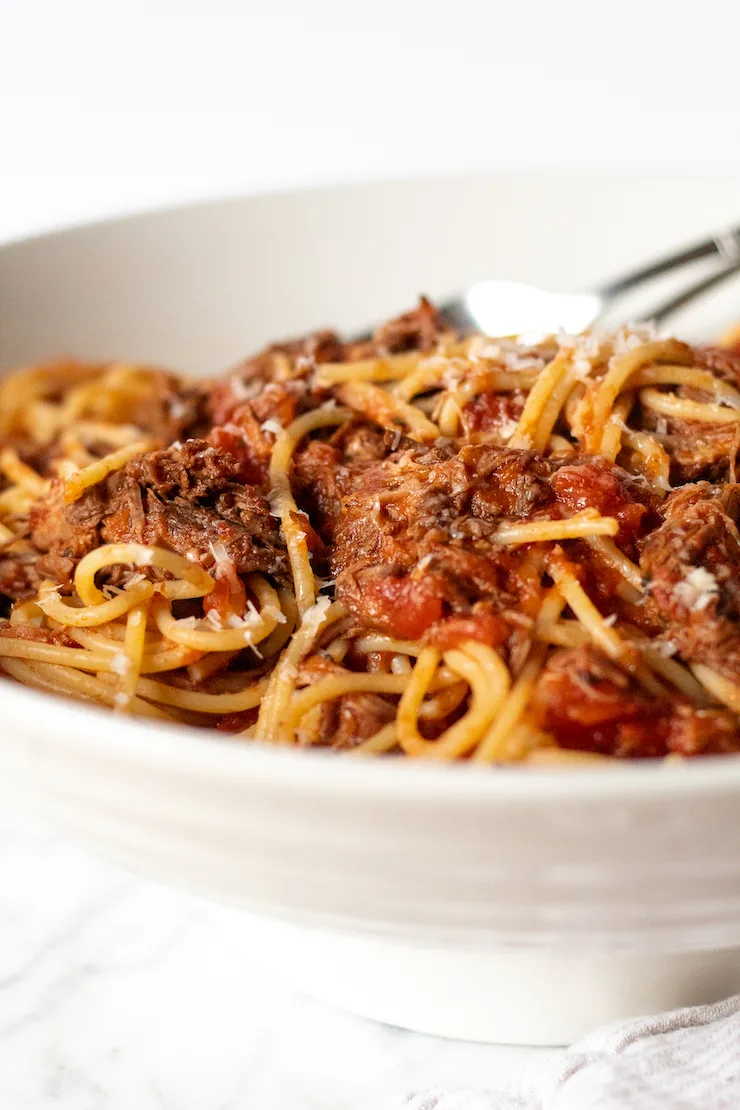 Sunday gravy tossed with spaghetti in serving bowl.