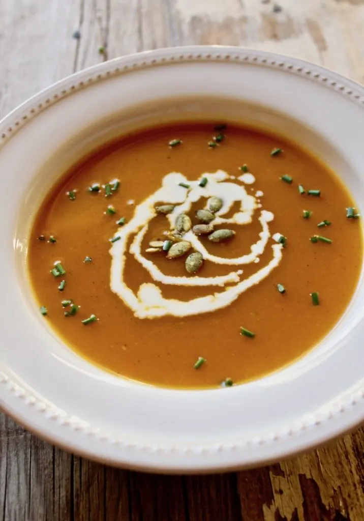 Autumn squash purée in serving bowl garnished with cream, pumpkin seeds and chives.