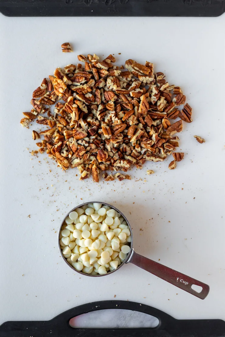 Chopped pecans and white chocolate chips on cutting board.