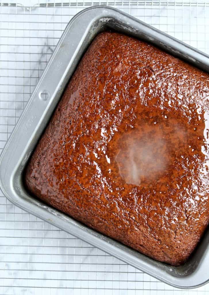 Gingerbread, warm with lemon glaze pooled in middle, on cooling rack.