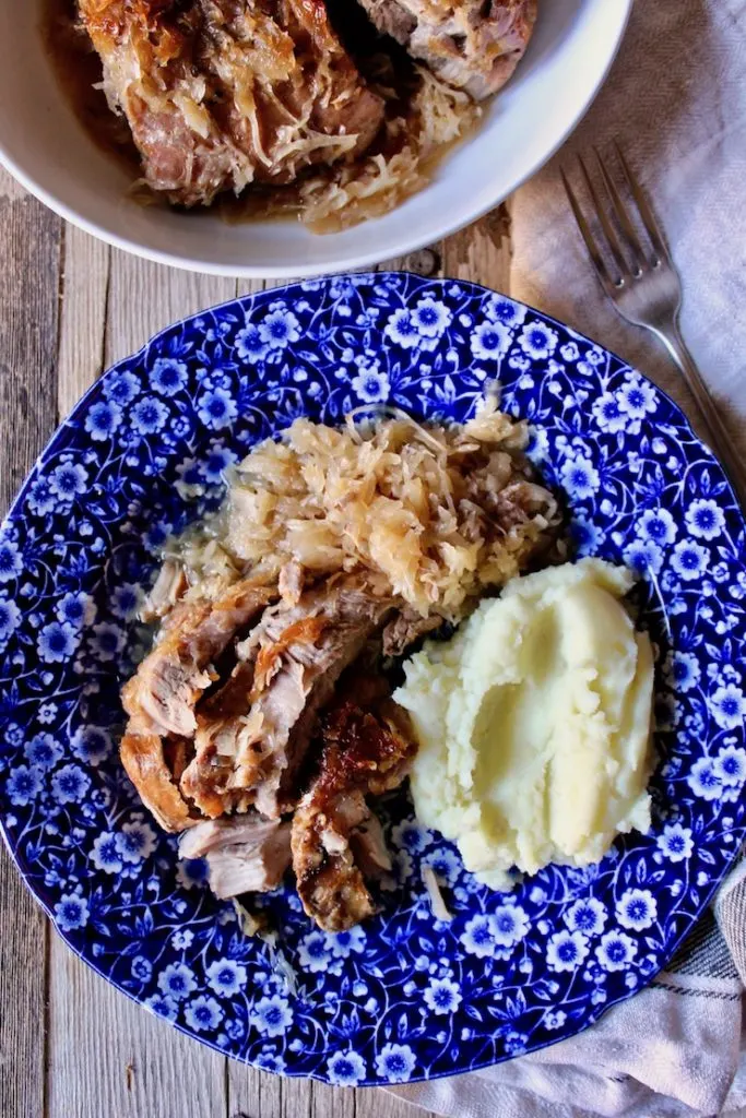 Finished braised pork on plate with mashed potatoes, serving bowl in background.