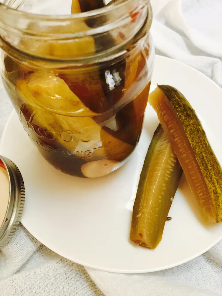 Open jar of pickles with two spears displayed on white plate.
