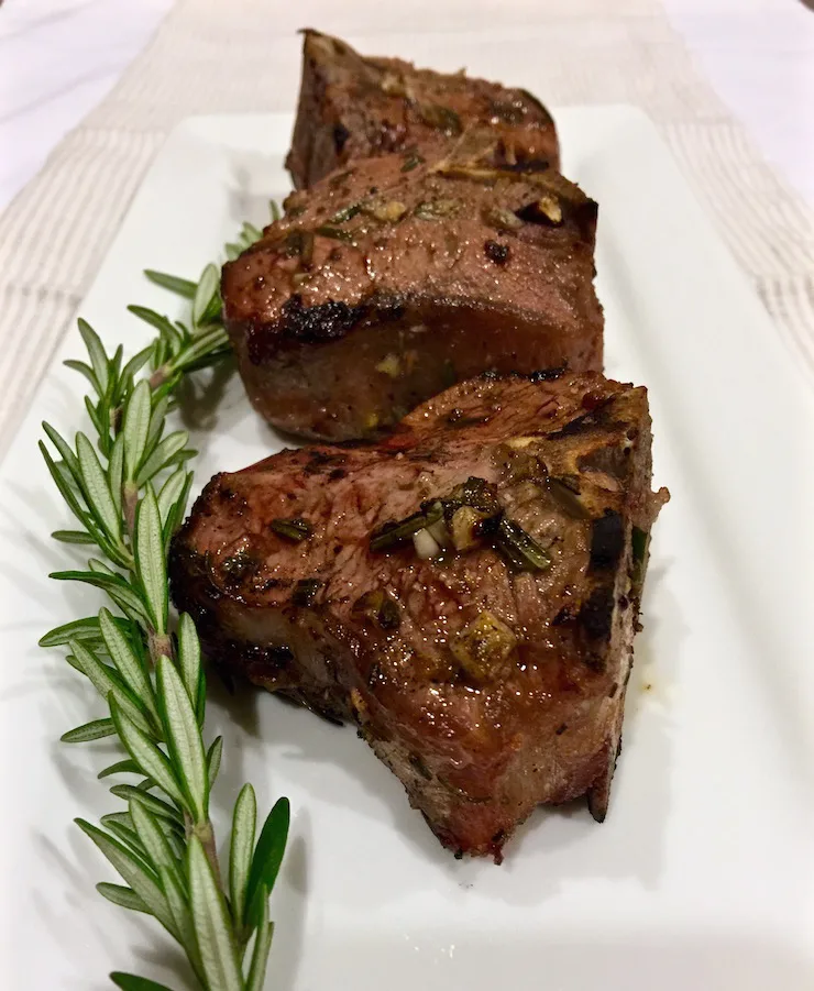 Grilled marinated lamb chops on white serving platter.