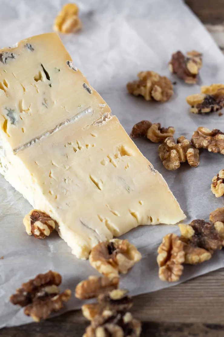 Wedge of gorgonzola cheese surrounded by walnuts.