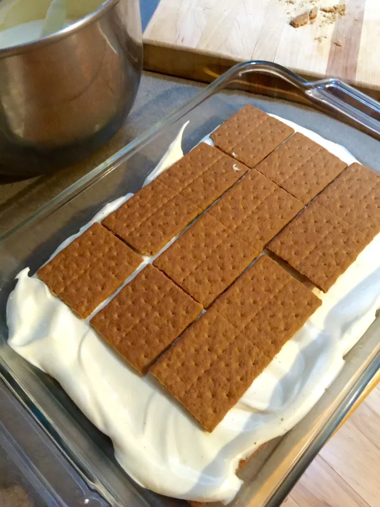 Éclair Cake, layering with graham crackers in glass dish.