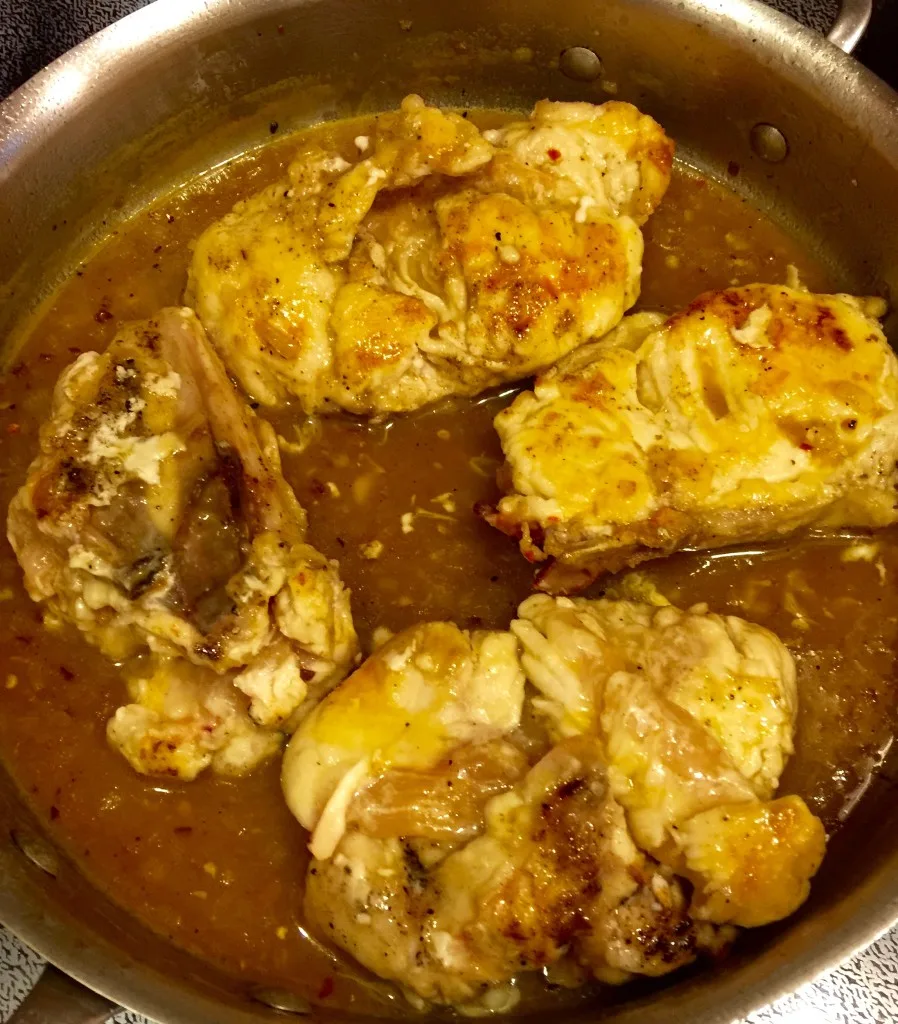 Chicken cooking in glaze in skillet.