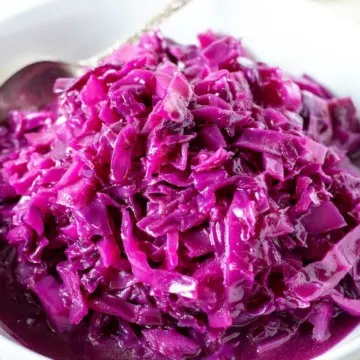 Red cabbage in white serving bowl with spoon.