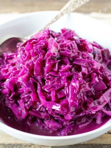 Red cabbage in white serving bowl with spoon.