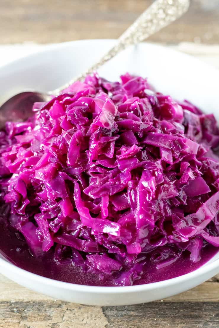 Red cabbage in white serving bowl with spoon.