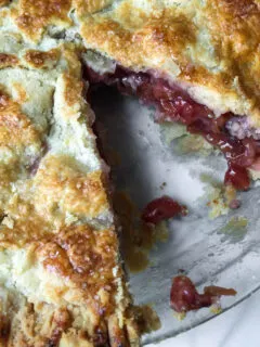 Overhead of cherry pie with piece missing, showing flaky crust and filling.
