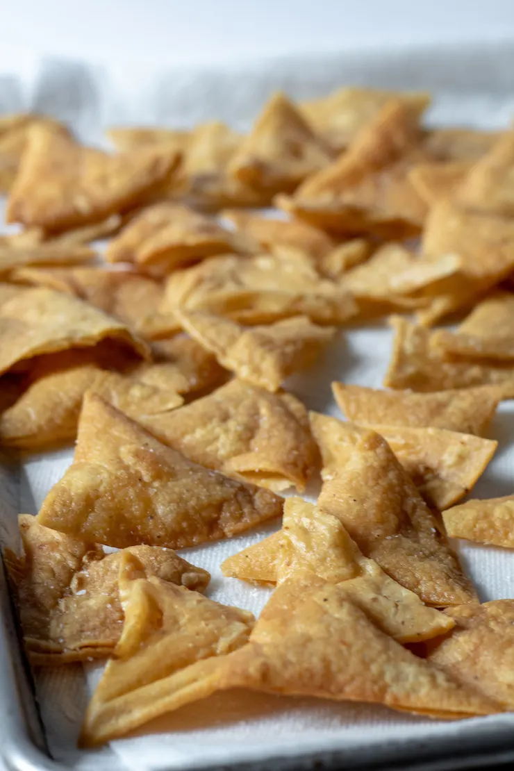 Homemade tortilla chips draining on paper towel lined sheet pan.