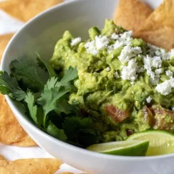 Guacamole in white bowl with crumbled fresh cheese and homemade chips.