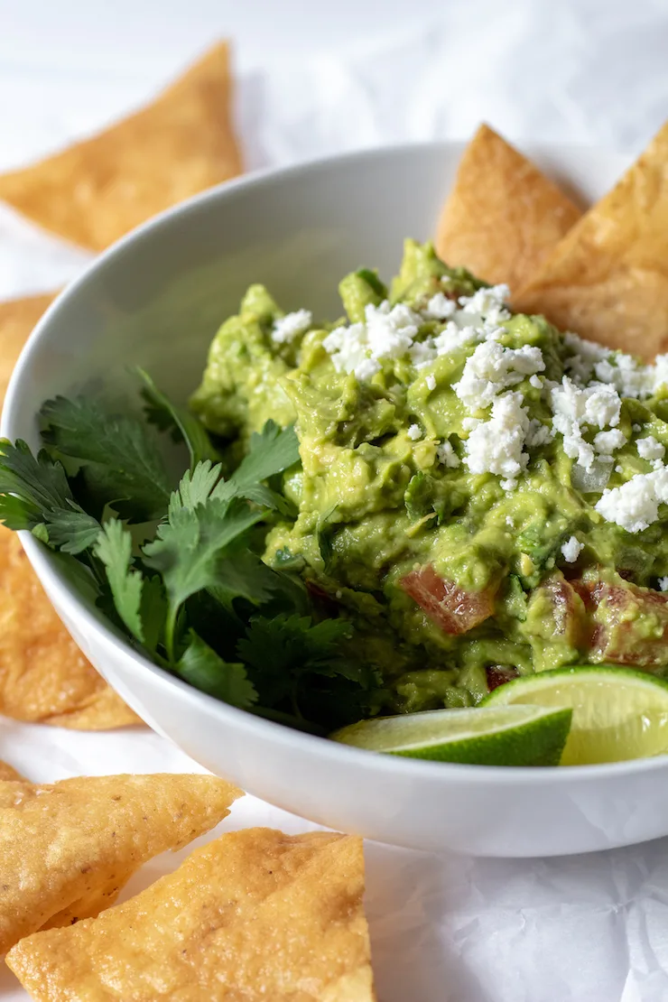 Guacamole in white bowl with crumbled fresh cheese and homemade chips.