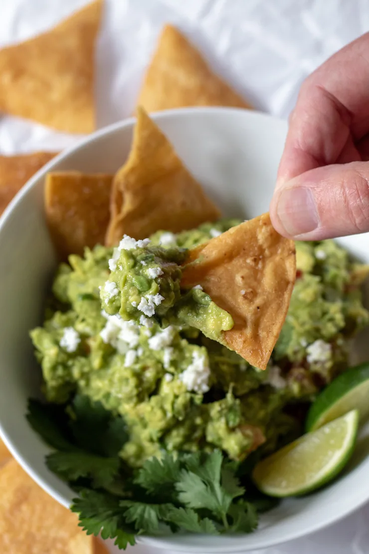 Hand dipping a chip in guacamole.