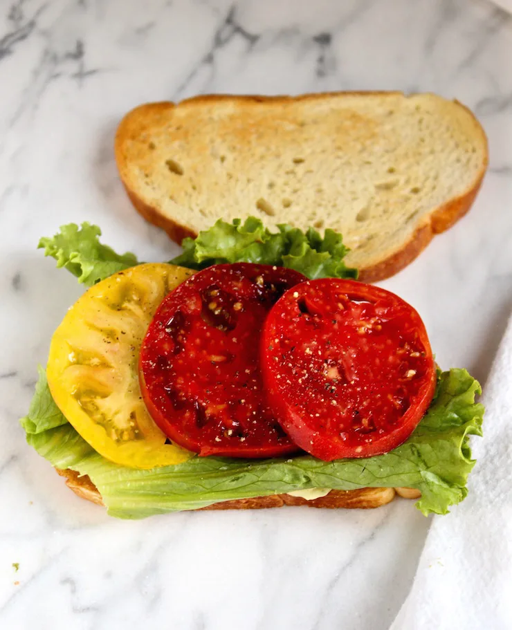 Open faced start of BLT with tomato and lettuce.