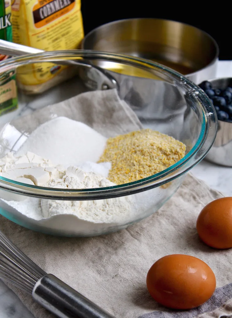 Ingredients in mixing bowl, eggs, melted butter and blueberries on side