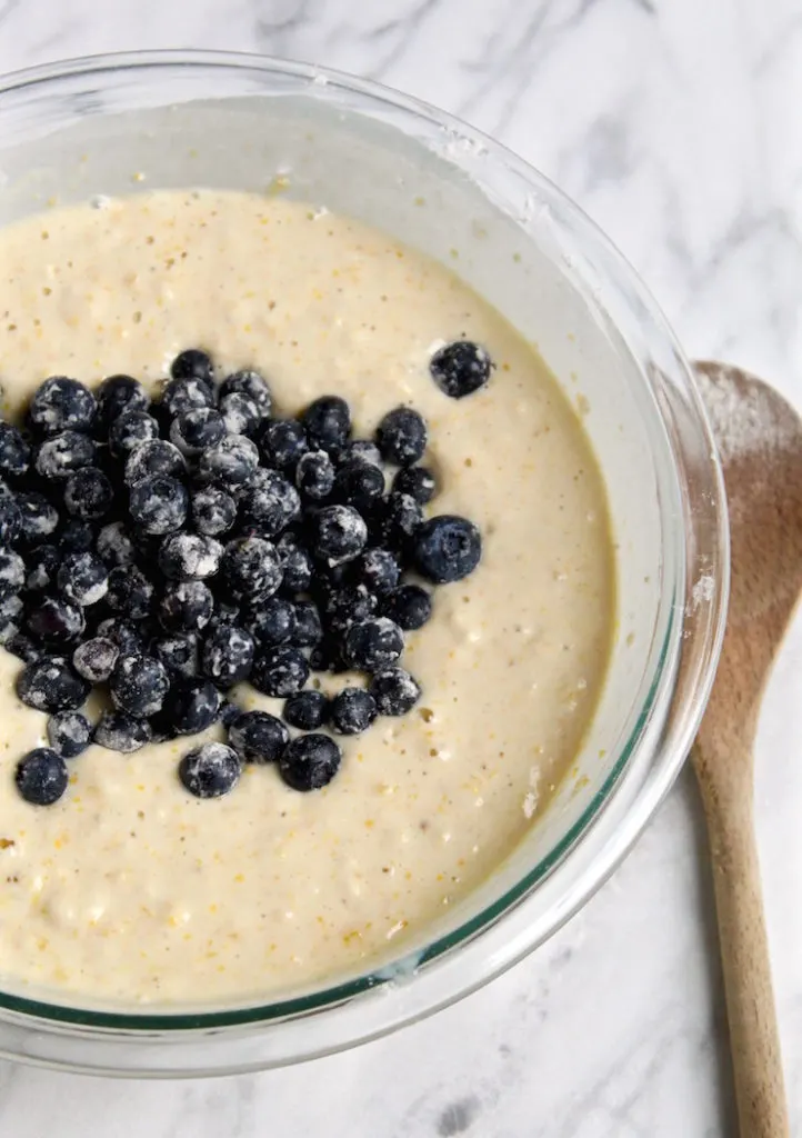 Blueberries scattered on top of batter with wooden spoon.