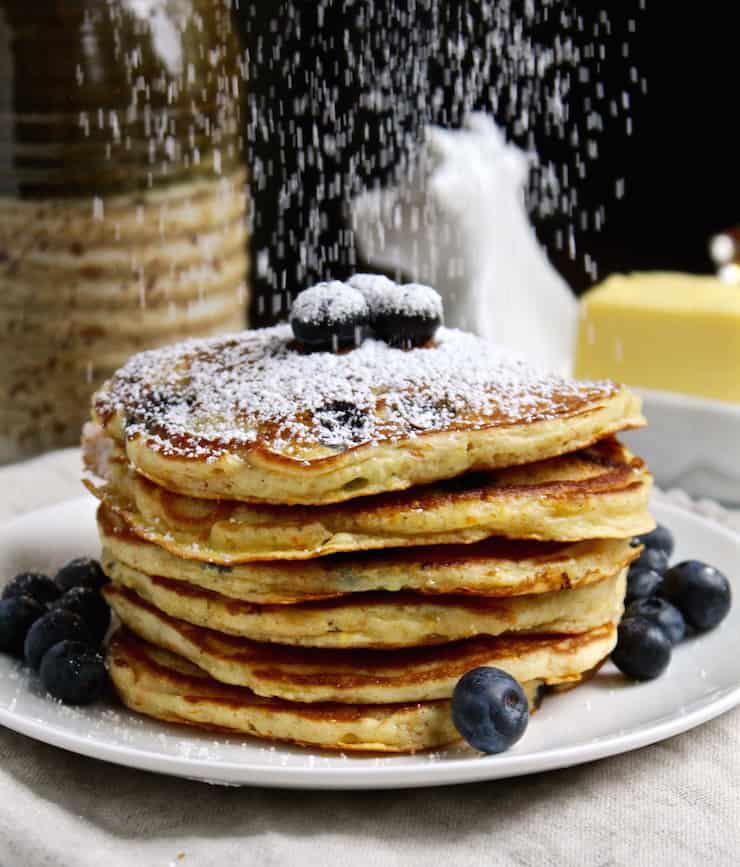 Cornmeal Blueberry Pancakes on plate with powdered sugar showering down over them.