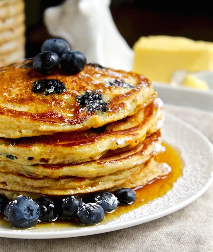 Cornmeal Blueberry Pancakes, side view of stack of pancakes with butter and syrup.