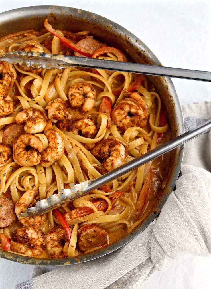 Creamy Cajun Shrimp Pasta with Sausage in skillet with tongs