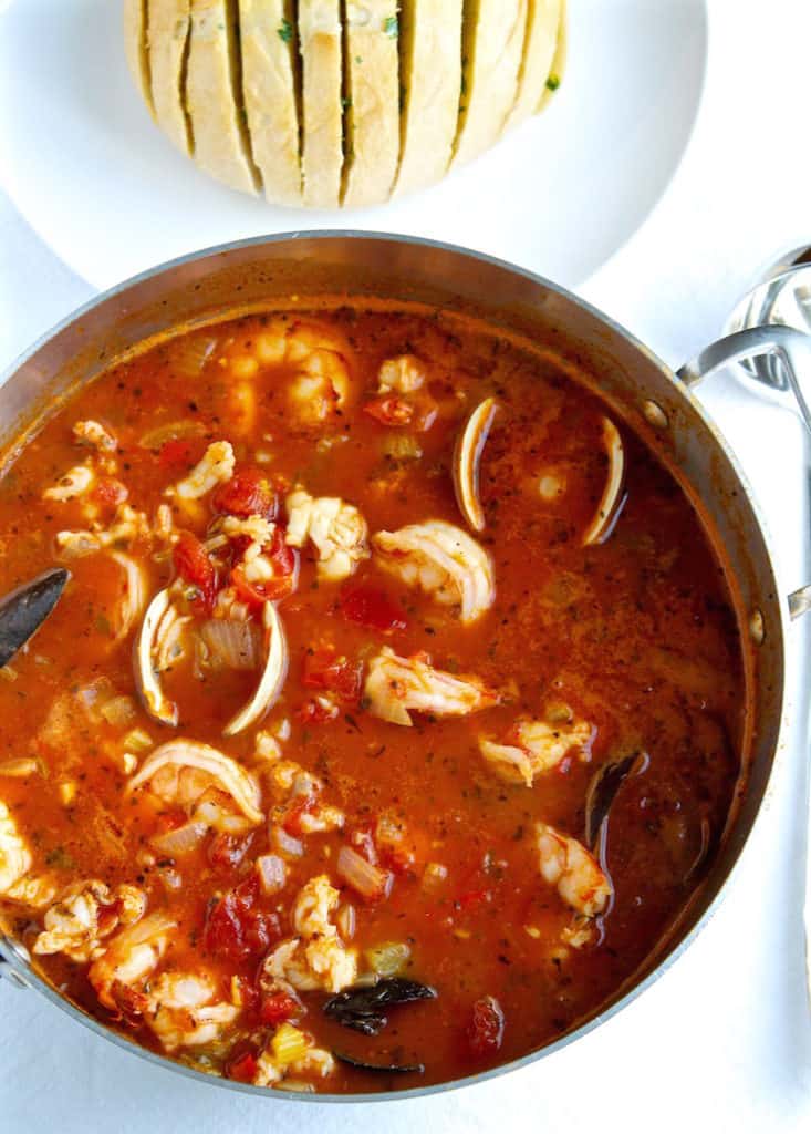 Pot of cioppino with sourdough bread in background