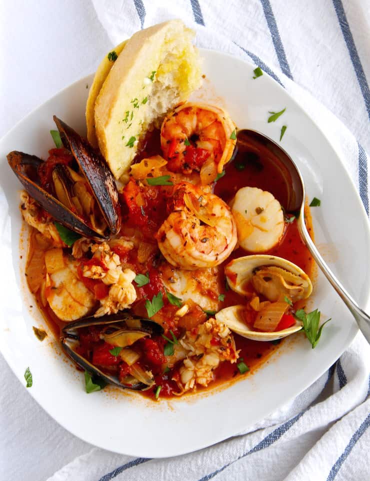 Cioppino in serving bowl with spoon and sourdough bread.