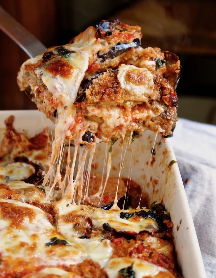 Eggplant Parmesan, serving piece with melty, gooey cheese out of baking dish